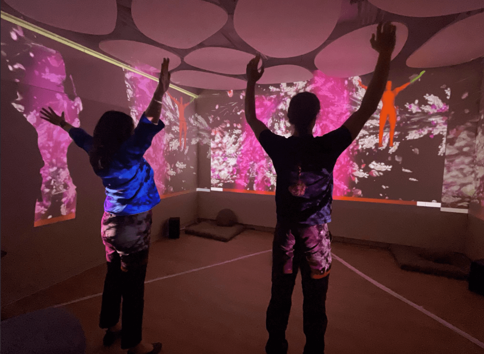 Two people following the movement guide projected on the surrounding walls in Breakthru’s Wellbeing Room.